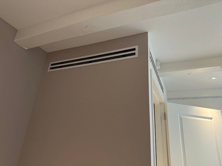 Strak weggewerkt inbouwrooster van een kanaalinbouw-airco tegen een gestucte wand
